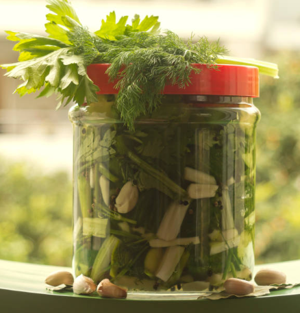 green vegetables fermenting in a plastic jar with red lid food grade container on windowsill